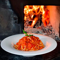 espaguetti boloñesa con plato de porcelana blanco, fuego de horno de leña